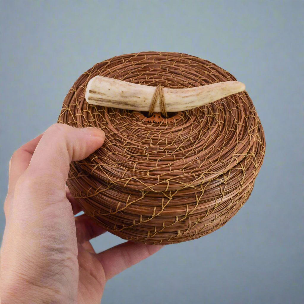 Pine needle basket with antler shown in hand for scale