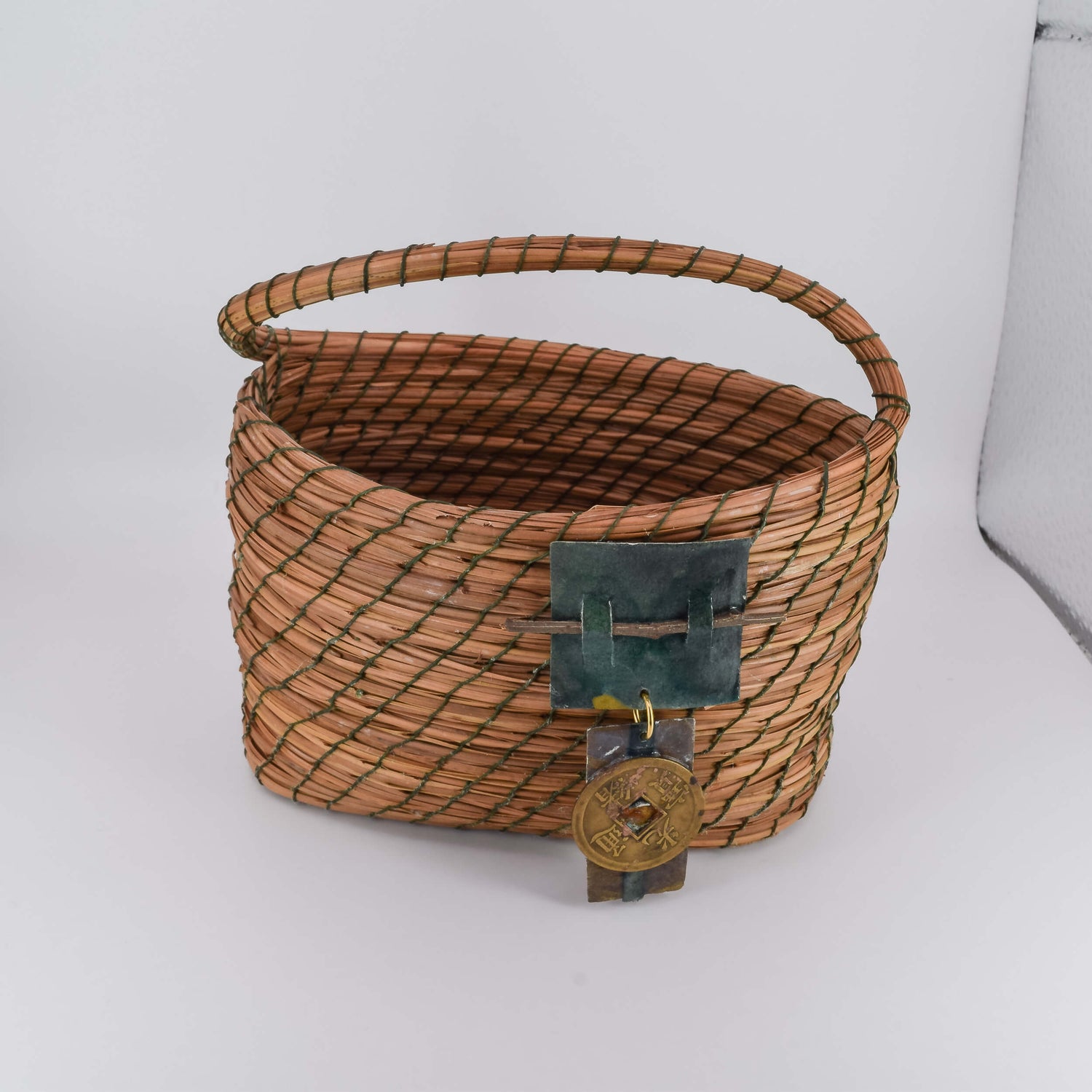 An oval pine needle basket with a handle and a metal ornate detail in front.