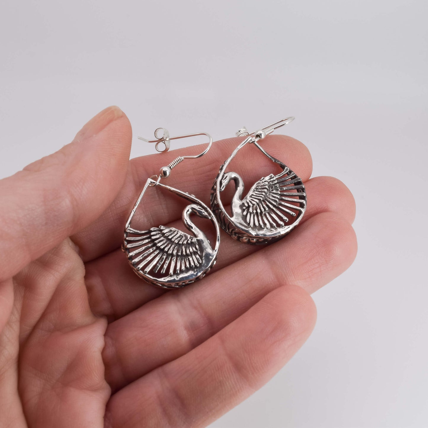 swan earrings in sterling silver shown in hand for scale